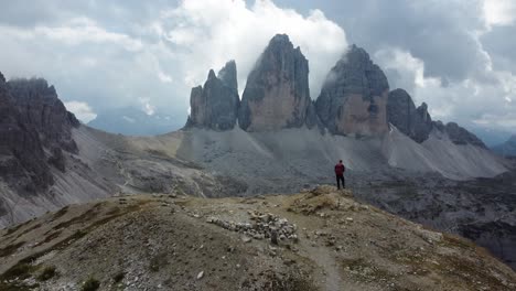 un excursionista parado solo en las montañas de los dolomitas en italia mirando tre cime di lavaredo en un día nublado