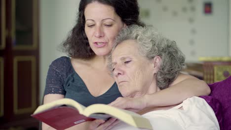 hija y madre leyendo un libro en la sala de estar, abrazándose