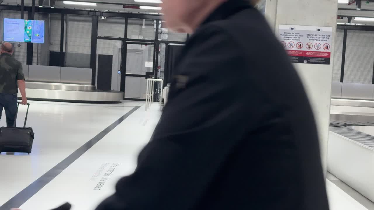 Man retrieves rolling suitcase from conveyor belt in modern, brightly lit airport baggage claim area