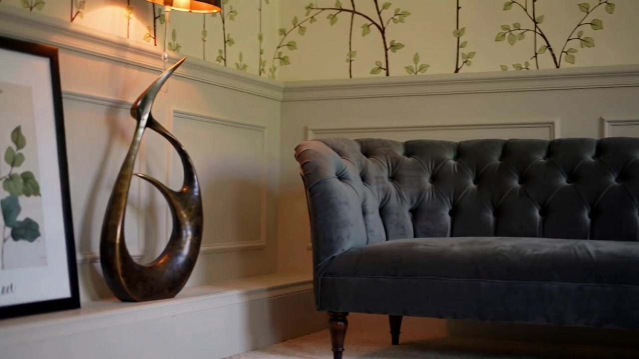 Panning camera moving right, revealing tufted grey sofa in parlor, showcasing sofa and leaf prints