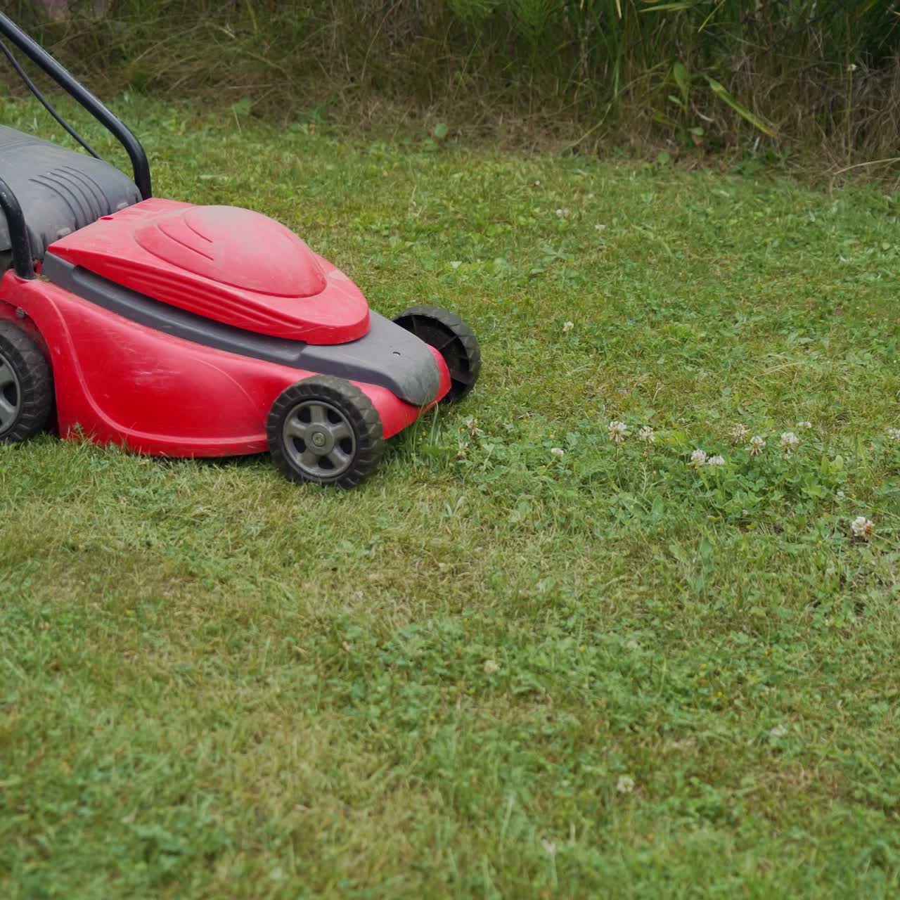 Barefoot young girl mowing grass with a lawn mower in garden. Bare female feet walking behind lawn mower in back yard