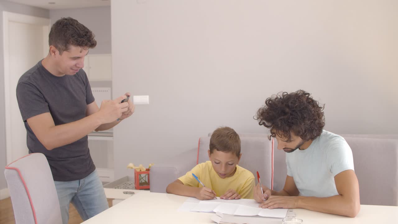 Niño concentrado haciendo los deberes escolares con la ayuda de sus dos papás.