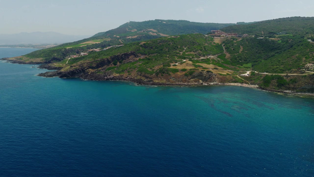 Riprese aeree con drone della costa frastagliata della Sardegna settentrionale, Italia. Acque cristalline del Mediterraneo, colline verdi, scogliere rocciose e paesaggi costieri incontaminati in una soleggiata giornata estiva