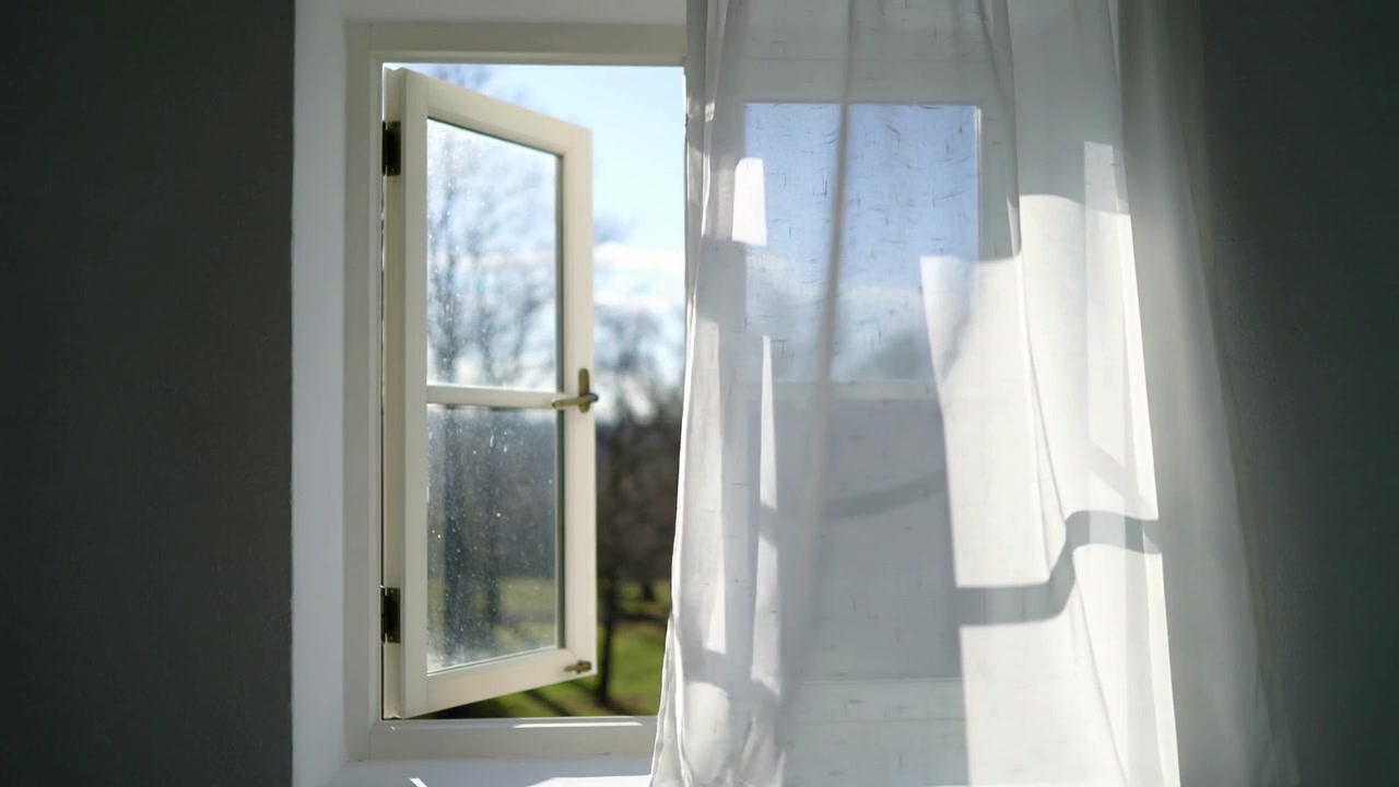 Billowing sheer curtain moving across white window with left-open sash in light room from breeze