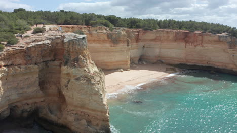Aerial-of-a-small,-beautiful-sand-beach-surrounded-by-tall-cliffs