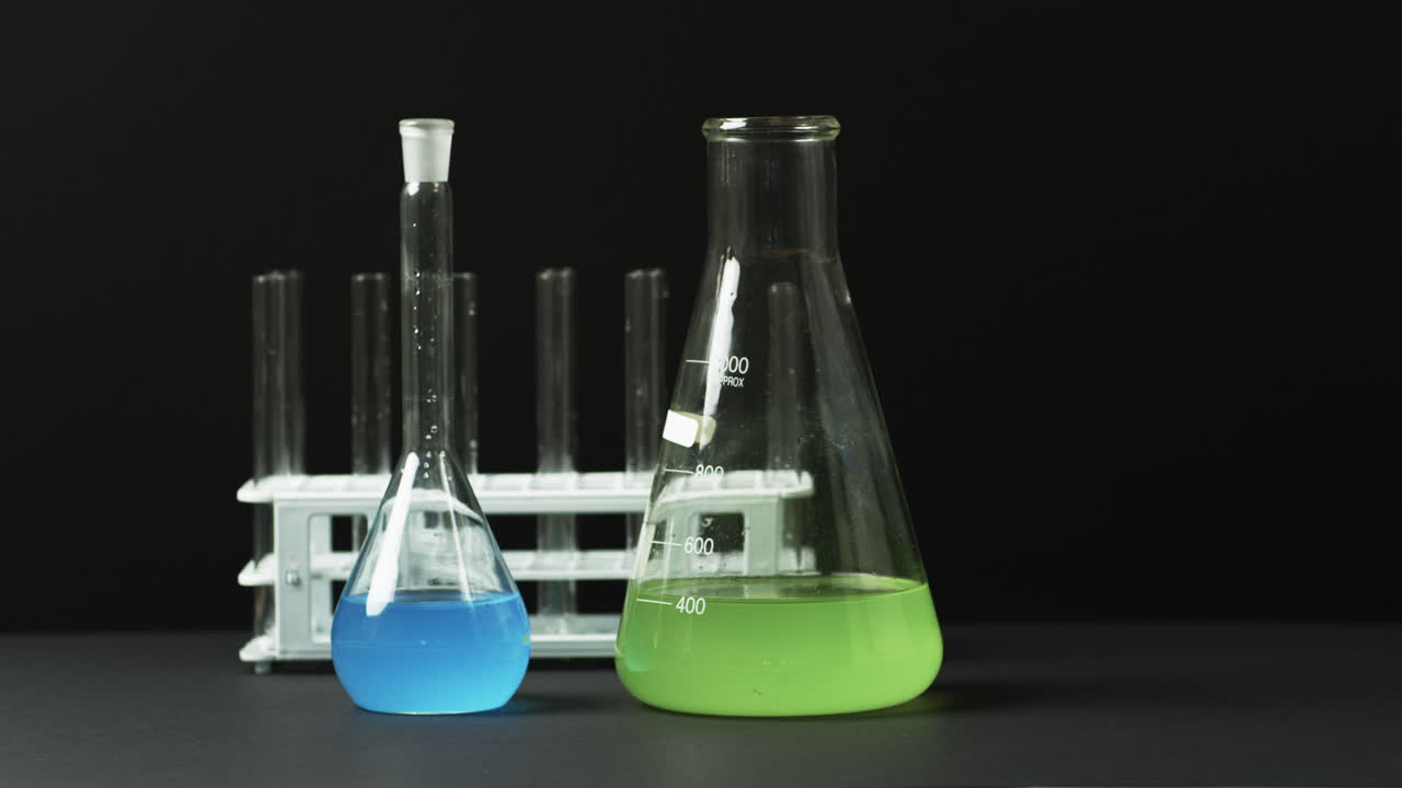Coloured liquids in flasks and tubes depict a science lab setup in slow motion.