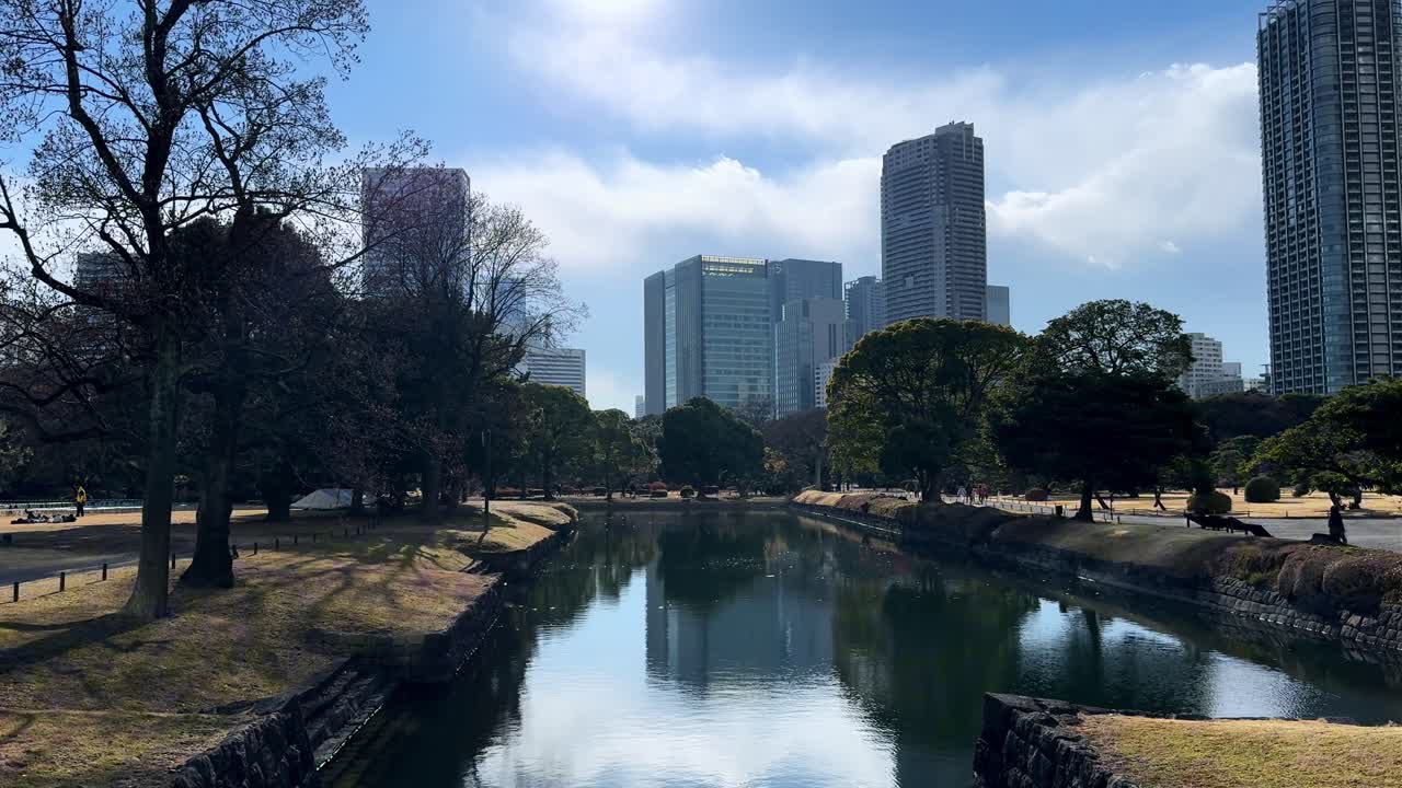 A calm canal view in Hama Rikyu Gardens, surrounded by trees and city skyscrapers