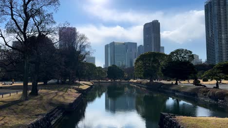una vista tranquila del canal en los jardines de hama rikyu, rodeados de árboles y rascacielos de la ciudad