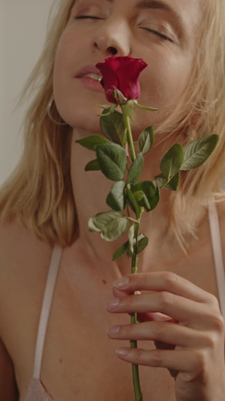 Ritratto sensuale di una bella donna bionda che annusa una rosa rossa, mentre indossa della lingerie.