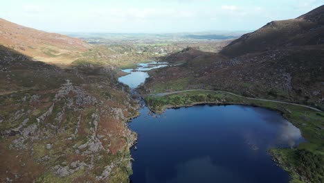 wide panning aerial shot of gap of dunloe, bearna or choimín, mountain pass in county kerry, ireland, with a bridge over the river loe