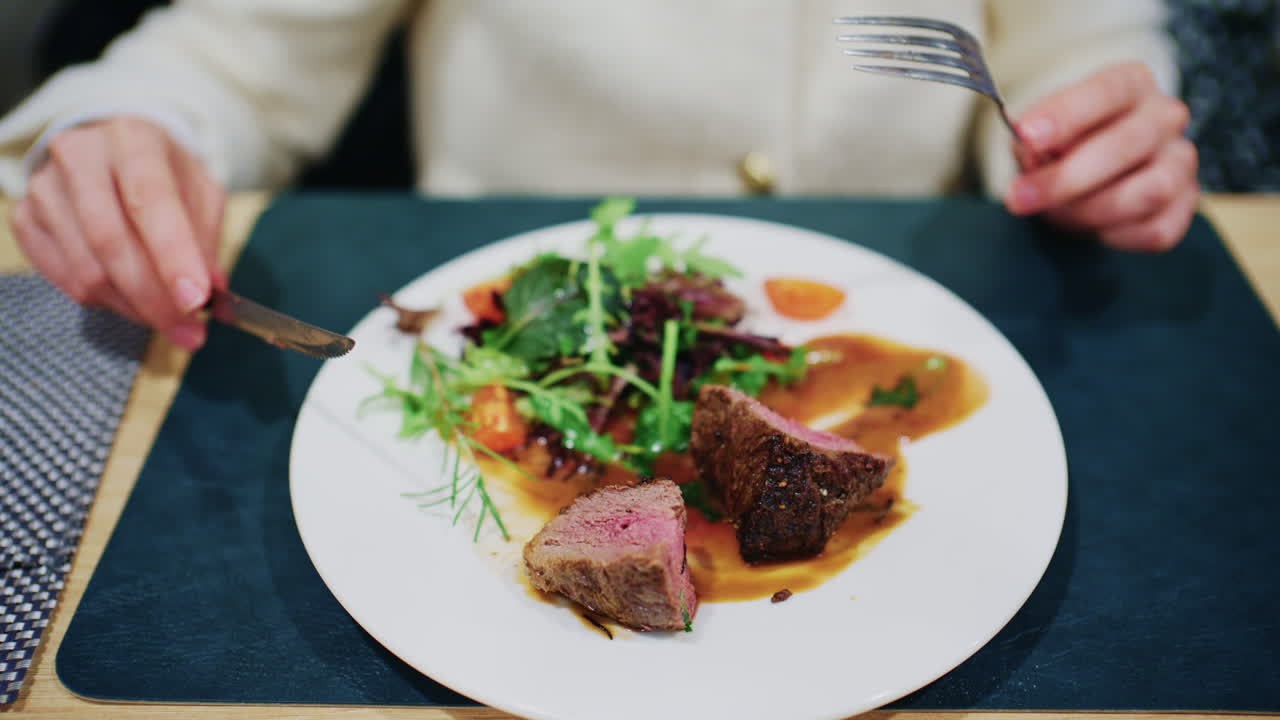 Woman cutting a medium rare steak served with vegetables and sauce on a restaurant plate
