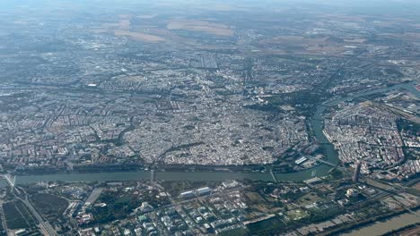 Elevated-spinning-aerial-view-of-Seville-city,-Spain,-shot-in-the-morning-light-from-an-airplane-cabin