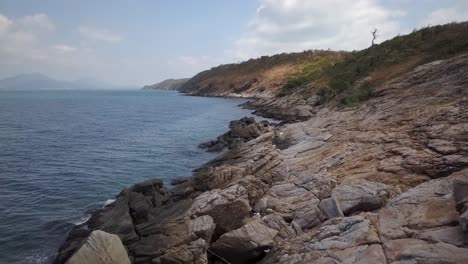 Aerial:-slow-forward-shot-over-the-rocky-shore-and-the-ocean-with-a-beautiful-landscape-and-an-island-in-the-distance,-Thailand