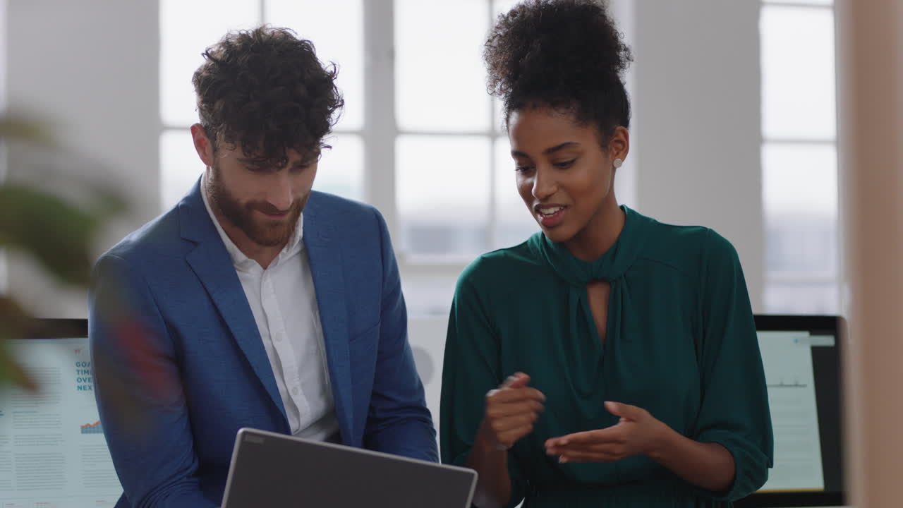 mixed race business woman team leader brainstorming with businessman colleague using laptop computer showing ideas pointing at screen working together in office
