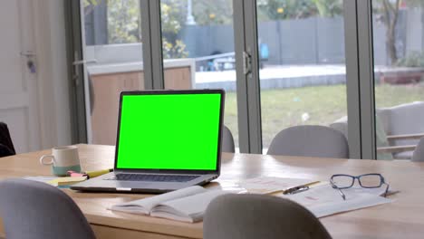 laptop with green screen, glasses and paperwork on dining table, slow motion