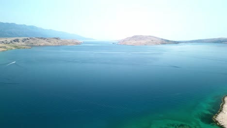 Una-Vista-Panorámica-Aérea-Sobre-El-Adriático-Azul-Y-La-Piedra-Blanca-Estéril-De-La-Isla-Pag,-Con-Una-Playa-Y-Un-Valle-Verde