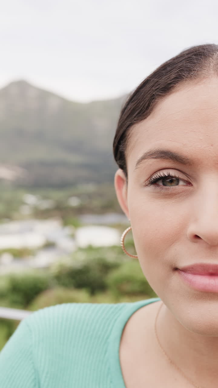 Vertical video of portrait of happy biracial woman standing on balcony at home, slow motion