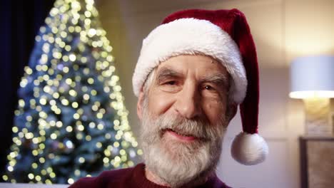 cerca de feliz viejo jubilado en santa hat videochatting en casa con árbol de navidad decorado brillante