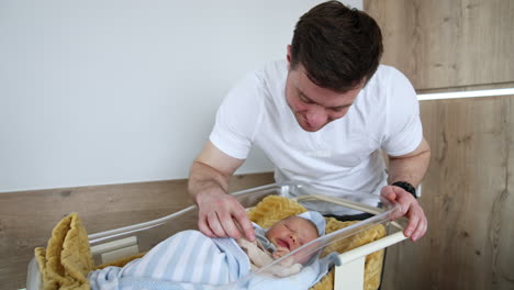 new-made father carefully unwraps little hands of his newborn child. dad strokes head and cheeks of a baby and kisses tenderly his kid.
