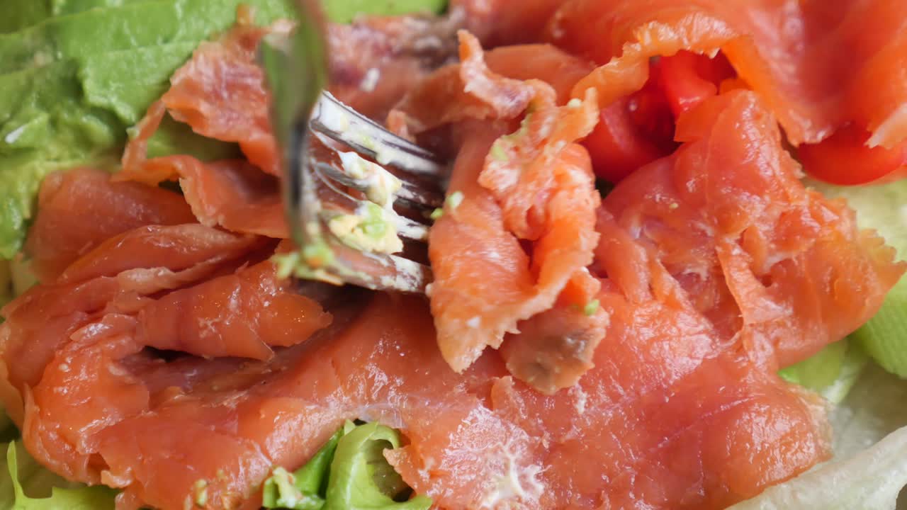 Forchetta che solleva salmone affumicato da un'insalata fresca