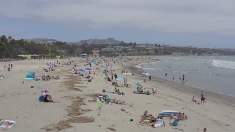 Eine-Schöne-Drohnenaufnahme-Aus-Der-Luft,-Die-Am-Strand-Entlang-über-Menschen-Fliegt,-Die-Ihren-Urlaub-Genießen,-Dana-Point---Orange-County---Kalifornien