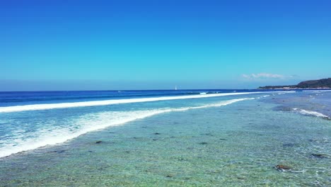 white waves splash and foam over shallow calm water of turquoise lagoon full of rocks and pebbles under clear open blue sky in malaysia