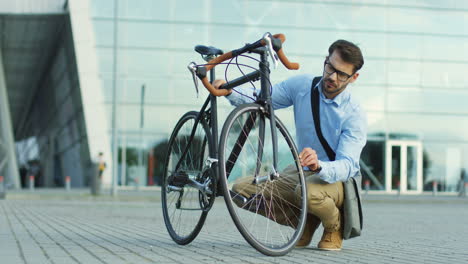 un joven elegante con un estilo informal revisando las ruedas de su bicicleta antes de montarla