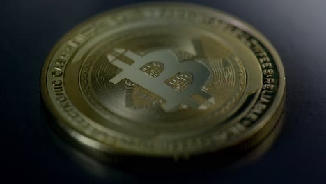 una moneta bitcoin d'oro fisica che giace sul tavolo scuro con un'ombra spazzata - ripresa macro