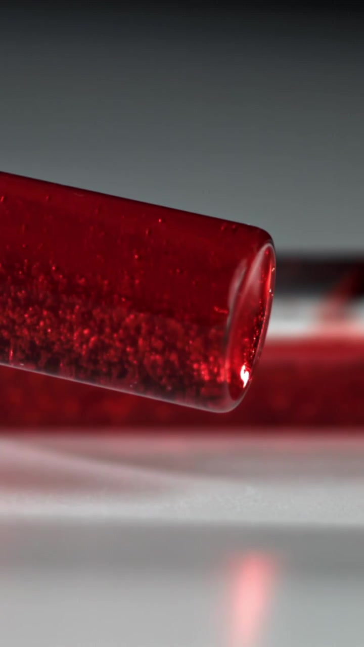 Red Glass Tube with Sparkling Particles on White Surface