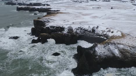 aerial view of strong waves crashing against steep coastline of arnarstapi, iceland in winter season