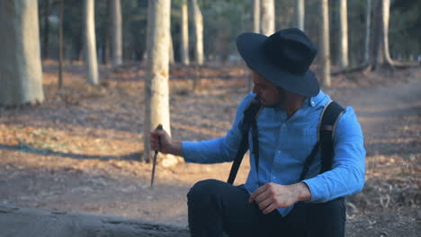 explorador clavando un cuchillo en un tronco y contemplando la naturaleza