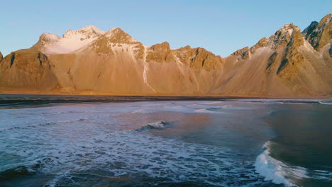 Vestrahorn-Mountain-sunrise-ocean-waves-aerial-view-reversing-across-Stokksnes-shore