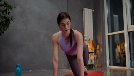 Confident-athletic-brunette-girl-in-purple-top-uses-video-tutorials-for-doing-sports-and-yoga-in-a-modern-apartment-on-the-Red-Mat.-Confident-brunette-girl-goes-in-for-sports-and-develops-using-online-lessons