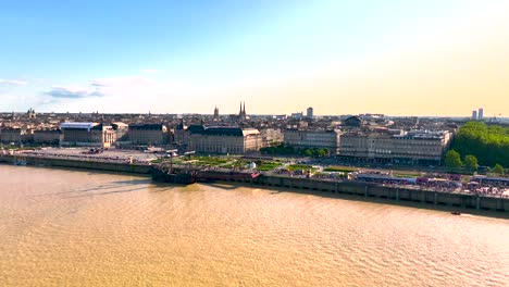 approaching place de la bourse plaza square in garonne river shore with large dark galleon ship in bordeaux france, aerial flyover shot