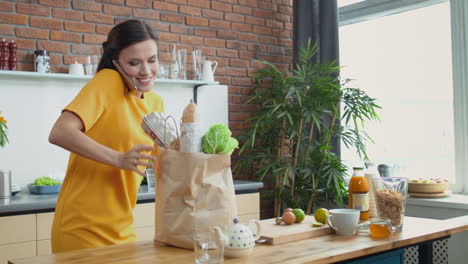 mujer volviendo a casa con bolsas de comestibles. chica bonita hablando por teléfono en la cocina.