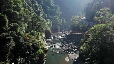 aerial flight of natural rocky stream and tourist walking over bridge during sunny day in national park of wulai district in taiwan,asia