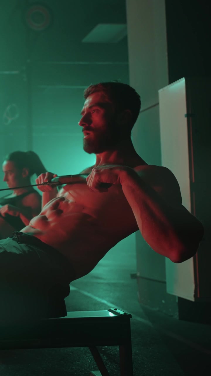 Uomo muscoloso che si allena su vogatore in palestra illuminata al neon