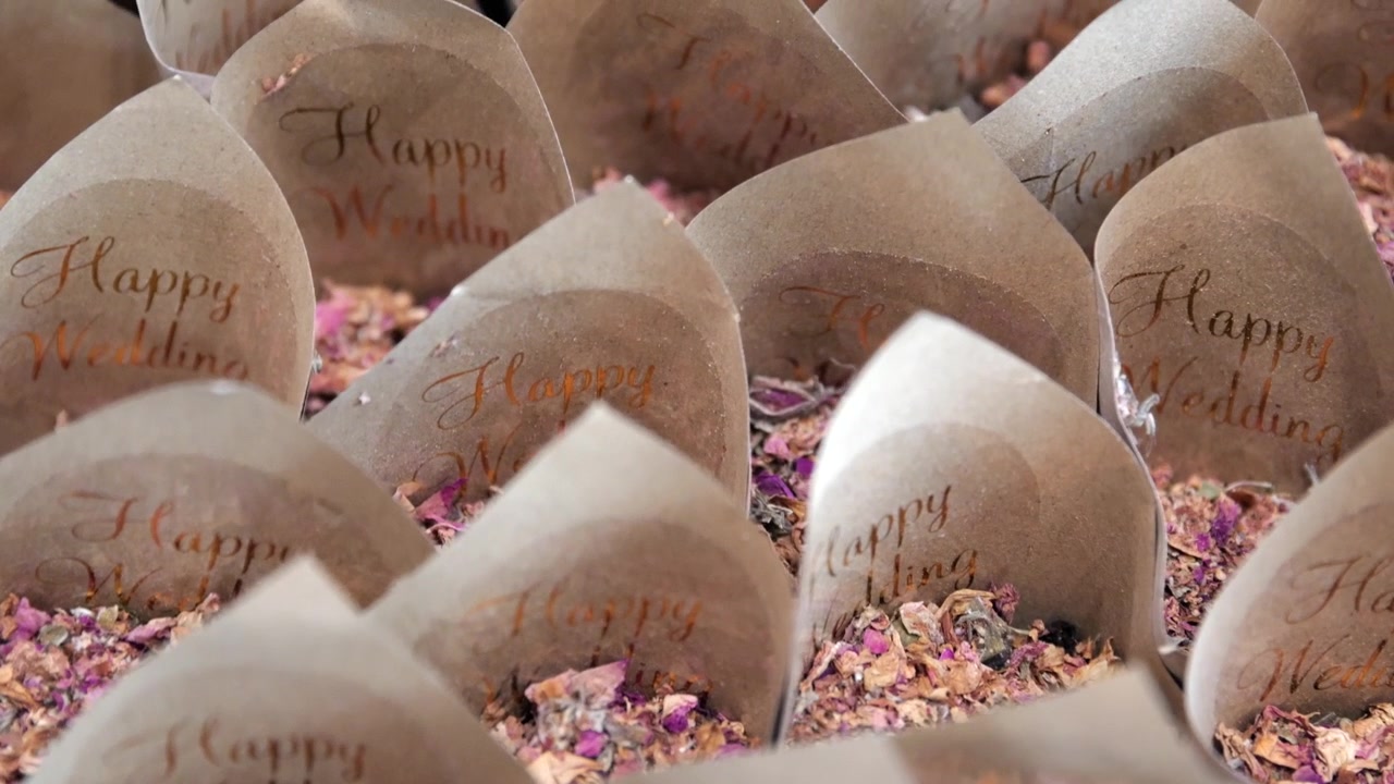 Handheld close-up of wedding petal cones with dried flowers and calligraphy