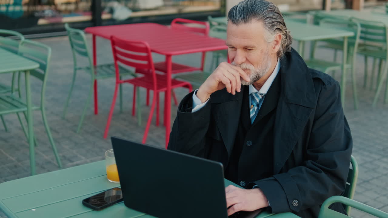 Forretningsmand, der arbejder på bærbar computer på udendørs cafe