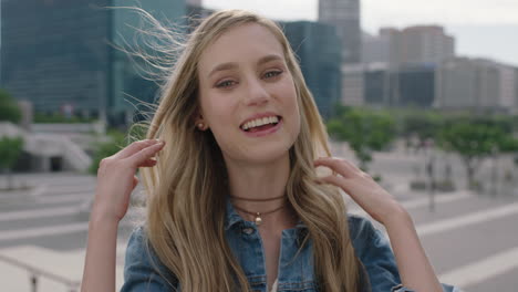 close up portrait of attractive blonde woman student smiling happy at camera running hand through hair in urban city enjoying lifestyle