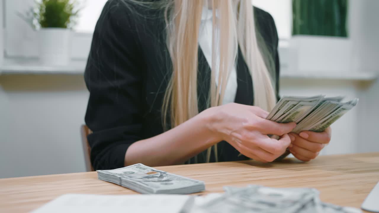 Деловая женщина, считающая наличные деньги в руках. Обрезать вид женщины в элегантном костюме, сидящей за деревянным столом и считающей большую пачку долларовых банкнот в руках.