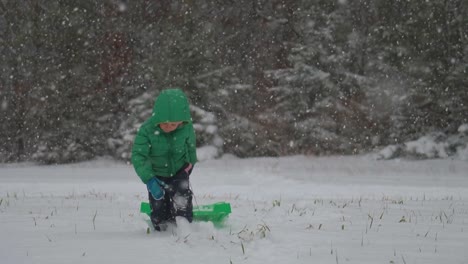 young boy pulling his sled through the snow with gently falling snow in slow motion