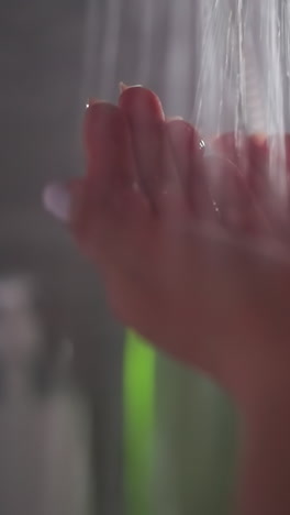 mujer encuentra consuelo en la suave cascada de agua caliente. mujer joven cubriendo las manos bajo el arroyo que fluye en la ducha. dama de pie bajo el agua caliente en la ducha