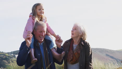 grandfather giving granddaughter ride on shoulders as they walk in countryside with grandmother