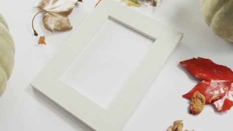 Empty-frame-with-copy-space,-pumpkin-and-autumn-leaves-against-white-background