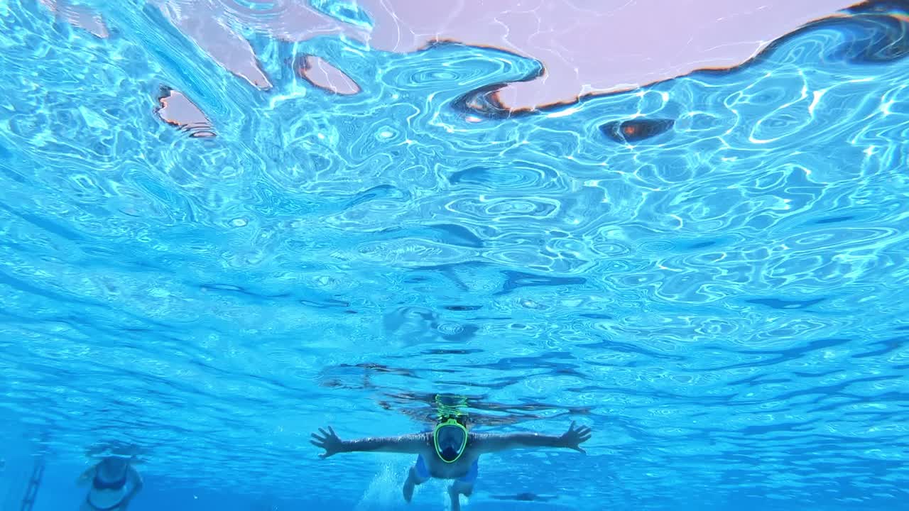 Man diving in mask in the pool. Blue transparent water and a strong male swimming under the water. Underwater video.