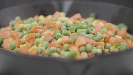 frozen peas and carrot rolling in to a pan for healthy organic vegetarian food diet preparation from a restaurant chef , close up of vegetable ingredients