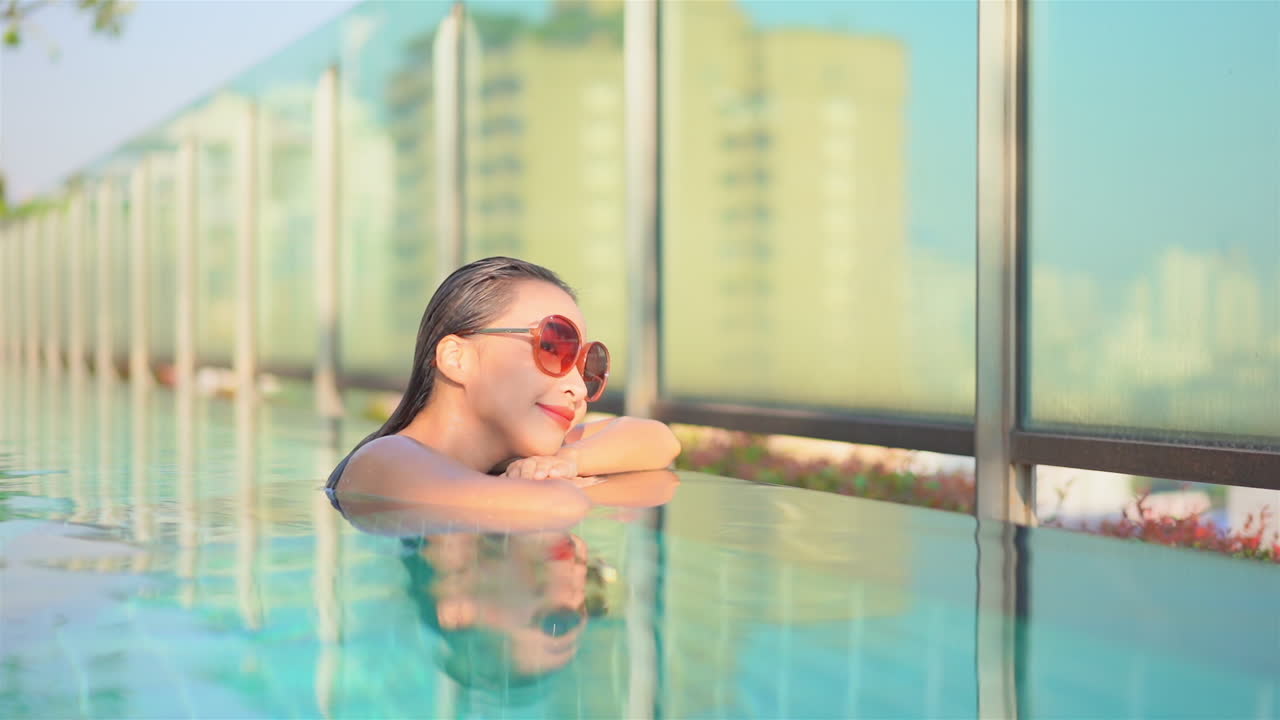 옥상 수영장에서 수영을 마친 젊은 여성이 도시 스카이라인을 바라보며 팔에 머리를 얹고 있습니다.