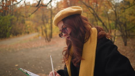joven con el cabello rojo ondulado en un parque tranquilo, centrado en la escritura en su cuaderno, rodeado de follaje de otoño vibrante en un entorno tranquilo
