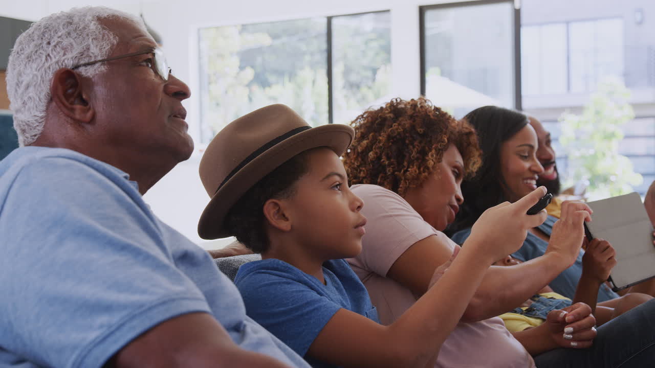 Multi-Generation African American Family Relaxing At Home Sitting On Sofa Watching TV Together
